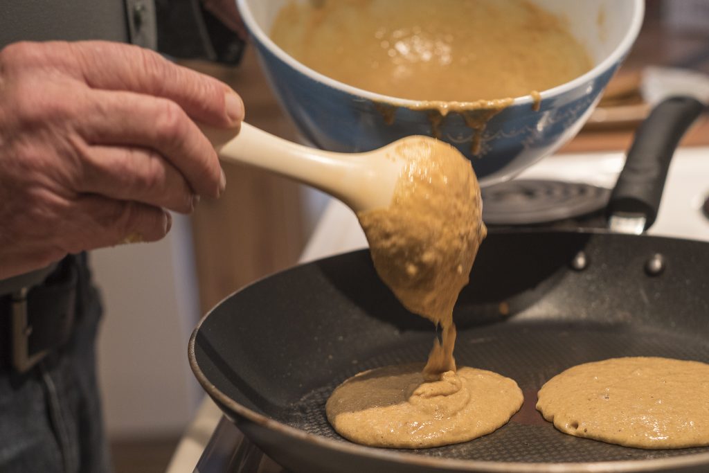 The batter has rested and the skillet is hot. Tom drops the batter with a ladle onto the skillet. 