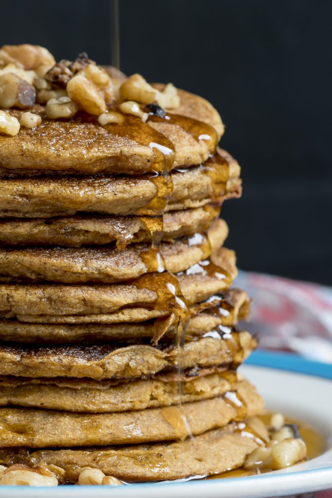 A stack of delicious pumpkin pancakes with maple syrup and walnuts.